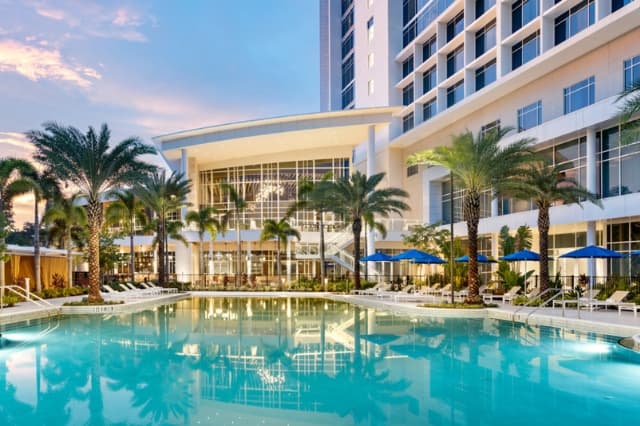 The illuminated outdoor swimming pool and modern exterior of the JW Marriott hotel at dusk.