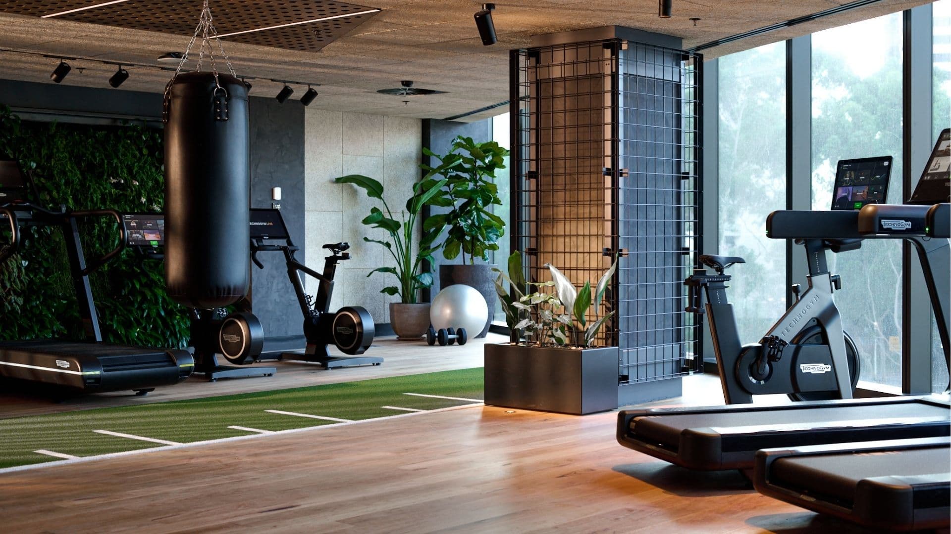 Modern hotel fitness center with a boxing bag, cycling and rowing machines, a living green wall, and a functional training turf area